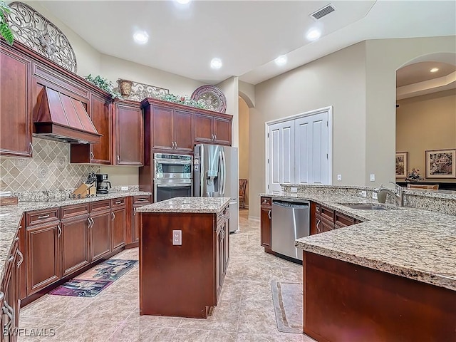 kitchen featuring arched walkways, stainless steel appliances, premium range hood, a sink, and a center island