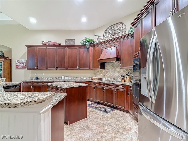 kitchen featuring decorative backsplash, a kitchen island, custom range hood, appliances with stainless steel finishes, and light stone counters