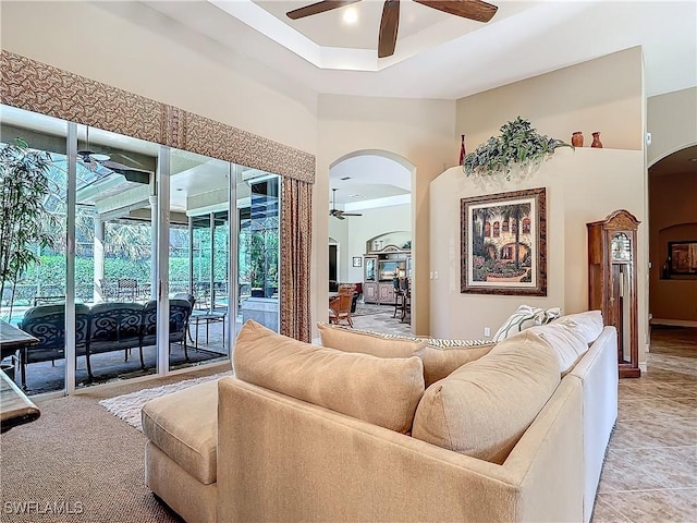 living area featuring arched walkways, ceiling fan, and a raised ceiling