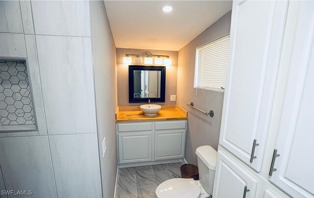 half bathroom with toilet, marble finish floor, and vanity