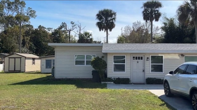 view of front of property featuring a storage shed, roof with shingles, an outdoor structure, and a front yard