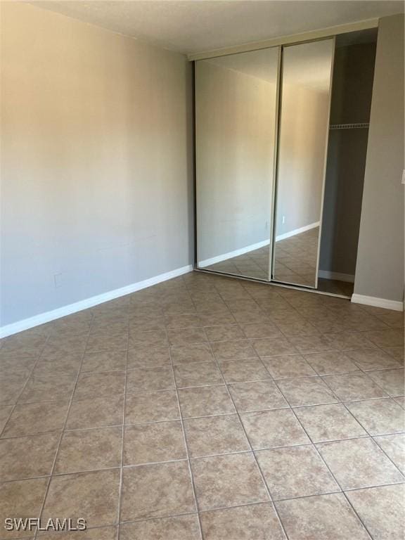 unfurnished bedroom with light tile patterned floors, a closet, and baseboards