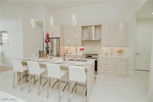 kitchen with appliances with stainless steel finishes, decorative light fixtures, a kitchen island with sink, wall chimney range hood, and a sink