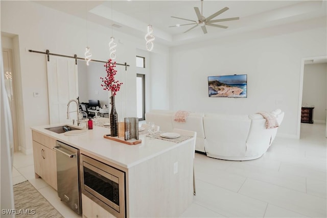 kitchen with a barn door, decorative light fixtures, a sink, appliances with stainless steel finishes, and a center island with sink