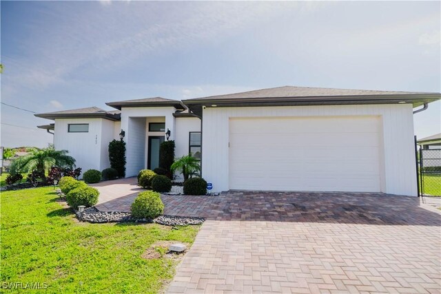 prairie-style home featuring an attached garage, a front lawn, and decorative driveway