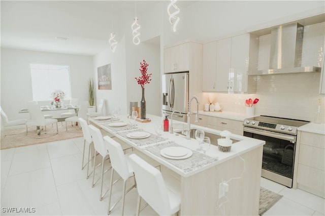 kitchen featuring light tile patterned floors, stainless steel appliances, white cabinets, light countertops, and wall chimney range hood