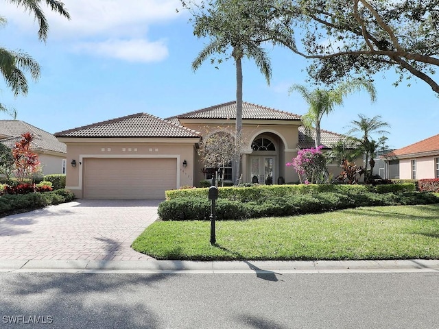 mediterranean / spanish home featuring a front yard, an attached garage, stucco siding, a tiled roof, and decorative driveway