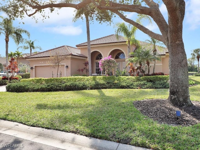 mediterranean / spanish-style home with a garage, a tiled roof, a front lawn, and stucco siding