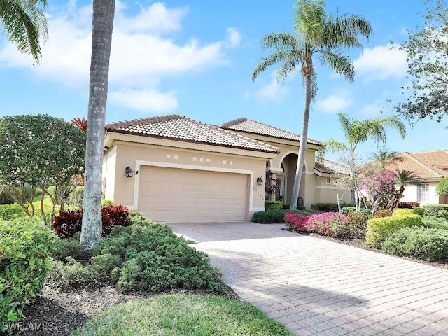 mediterranean / spanish house featuring an attached garage, a tile roof, decorative driveway, and stucco siding