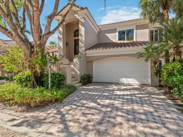 mediterranean / spanish-style house featuring a garage, decorative driveway, a tile roof, and stucco siding