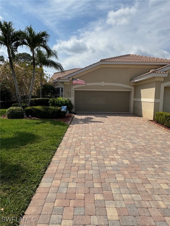 view of front of house featuring decorative driveway, a tile roof, stucco siding, an attached garage, and a front yard