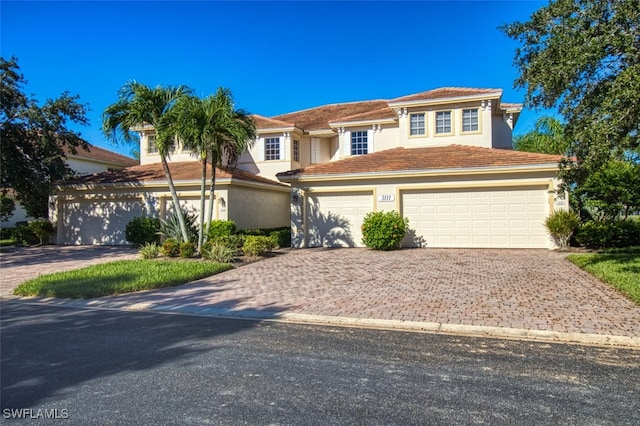 view of front of house with a tiled roof, decorative driveway, an attached garage, and stucco siding