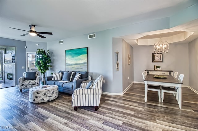 living room featuring ceiling fan with notable chandelier, visible vents, baseboards, and wood finished floors