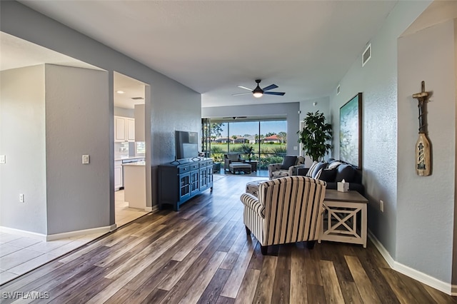 living room featuring a textured wall, dark wood-style flooring, a ceiling fan, visible vents, and baseboards