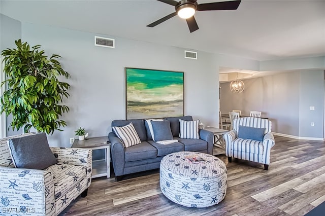 living room featuring ceiling fan with notable chandelier, wood finished floors, visible vents, and baseboards