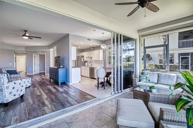 living room featuring light wood-type flooring, ceiling fan, visible vents, and baseboards