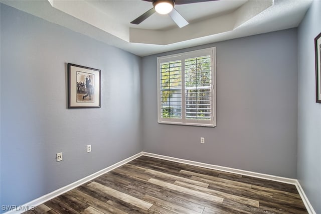 spare room featuring a ceiling fan, a raised ceiling, baseboards, and wood finished floors