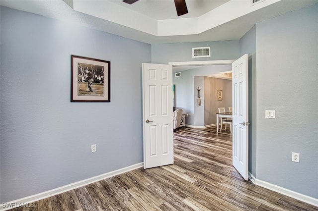 spare room with a raised ceiling, visible vents, a ceiling fan, wood finished floors, and baseboards