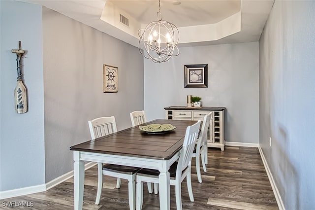 dining room featuring visible vents, dark wood finished floors, baseboards, a raised ceiling, and a notable chandelier