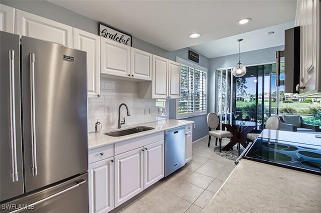 kitchen with tasteful backsplash, white cabinets, stainless steel appliances, pendant lighting, and a sink