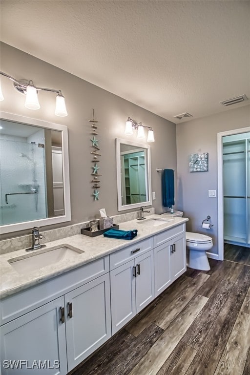 3111 Meandering Way Unit 101, Fort Myers, FL 33905 - bathroom with wood finished floors, a textured ceiling, double vanity, toilet, and an enclosed shower