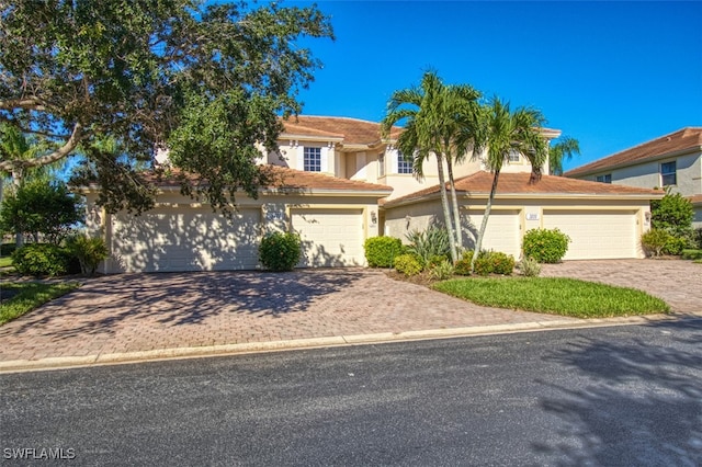 view of front of property featuring a garage, a tiled roof, decorative driveway, and stucco siding