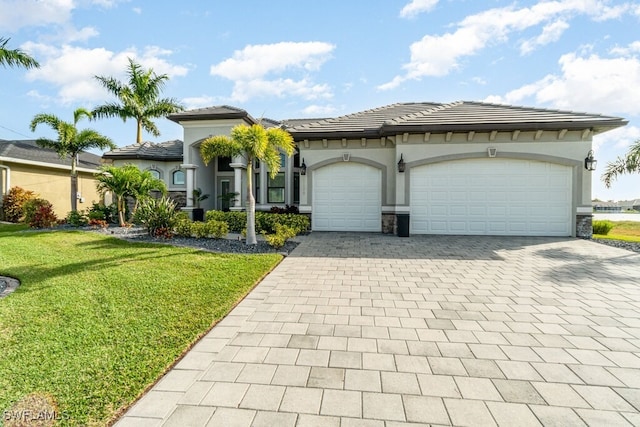 view of front of house featuring a tile roof, an attached garage, decorative driveway, a front lawn, and stucco siding