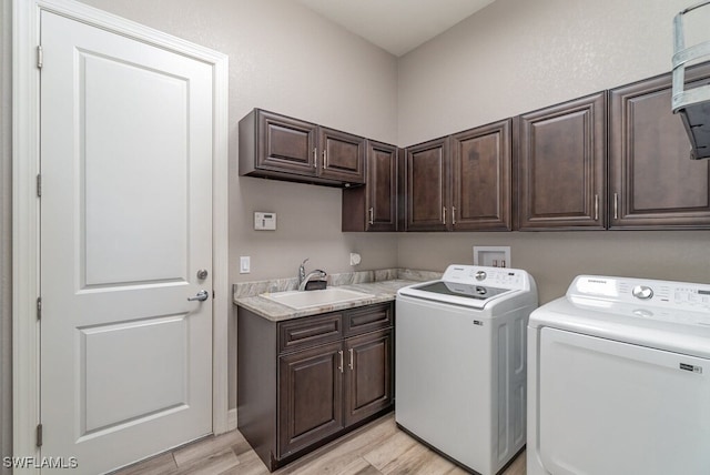 clothes washing area featuring light wood-type flooring, cabinet space, washer and clothes dryer, and a sink