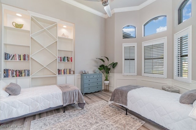 bedroom with light wood-type flooring, a wainscoted wall, ornamental molding, and a decorative wall