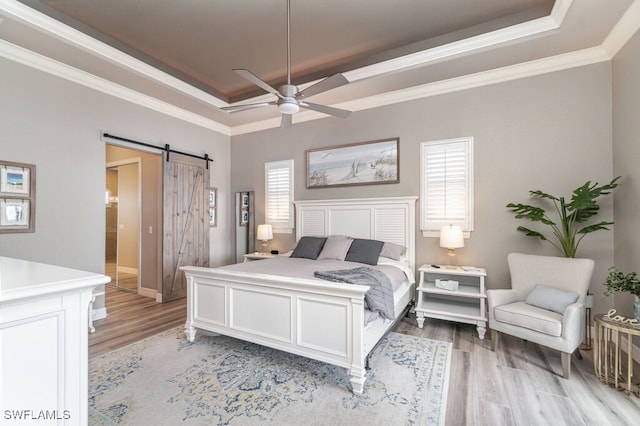 bedroom featuring light wood-type flooring, a tray ceiling, crown molding, and a barn door