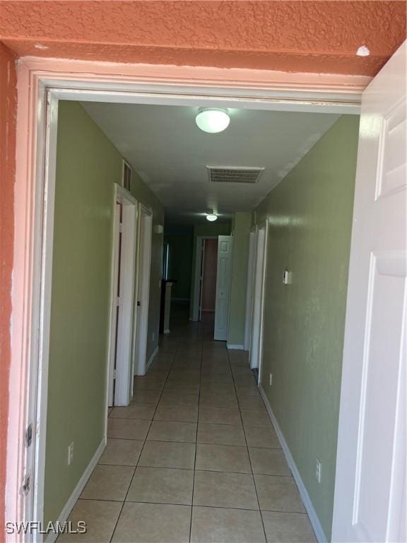 hallway featuring baseboards, visible vents, and light tile patterned flooring