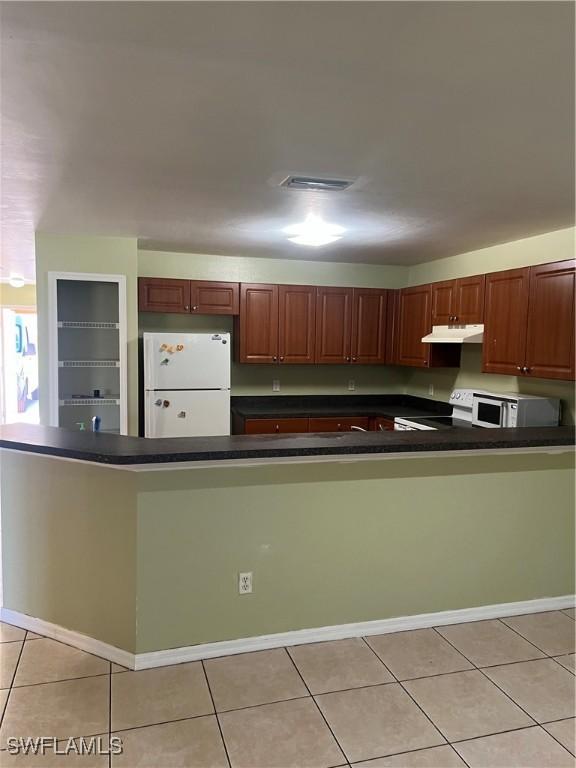 kitchen with light tile patterned flooring, under cabinet range hood, white appliances, visible vents, and dark countertops