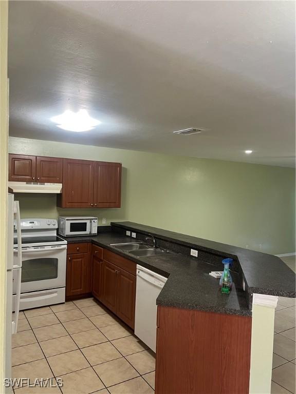 kitchen with light tile patterned floors, a sink, white appliances, a peninsula, and under cabinet range hood