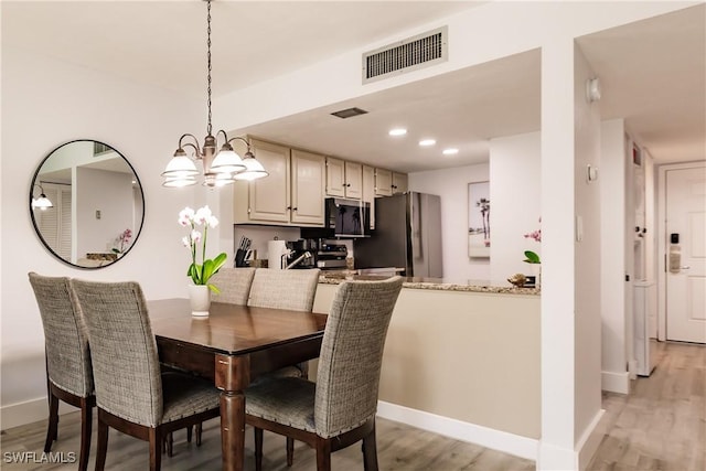 dining area with light wood-type flooring, visible vents, and baseboards