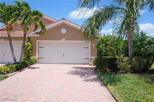 view of front of house with a garage, decorative driveway, a tile roof, and stucco siding