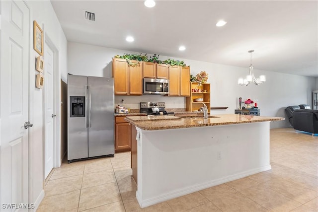 kitchen with pendant lighting, stainless steel appliances, visible vents, a kitchen island with sink, and light stone countertops