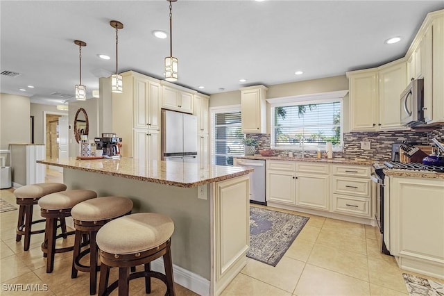 kitchen with light stone counters, a kitchen breakfast bar, cream cabinetry, appliances with stainless steel finishes, and decorative light fixtures