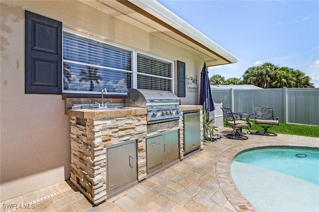 view of patio with an outdoor kitchen, a fenced in pool, area for grilling, fence, and a sink