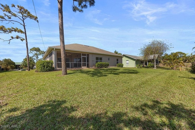 rear view of house with a lawn, a sunroom, and stucco siding