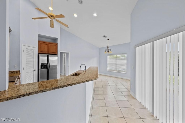 kitchen with brown cabinets, hanging light fixtures, stone countertops, light tile patterned flooring, and stainless steel fridge