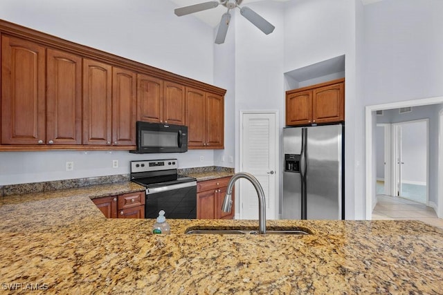 kitchen featuring stainless steel appliances, stone counters, a sink, and a towering ceiling