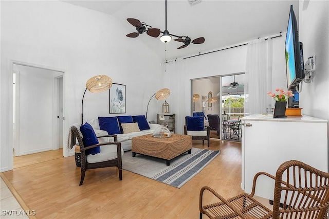 living room featuring light wood-type flooring, ceiling fan, a towering ceiling, and visible vents