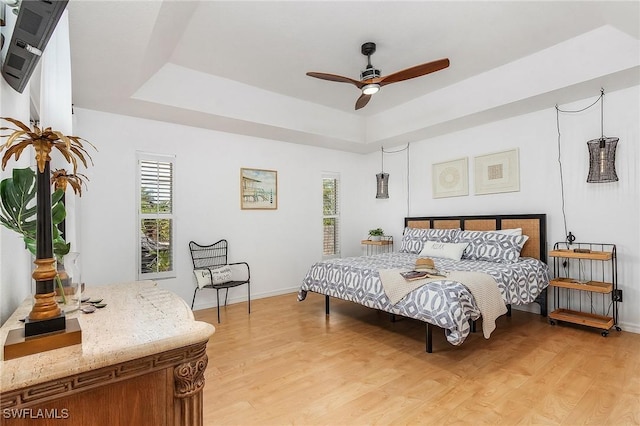 bedroom featuring light wood-type flooring, multiple windows, and a raised ceiling