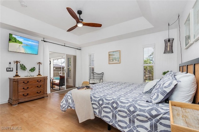 bedroom with a tray ceiling, access to outside, ceiling fan, and light wood-style flooring