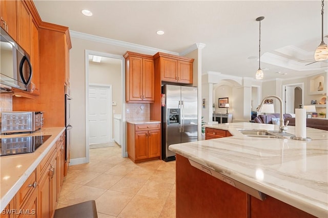 kitchen featuring brown cabinets, hanging light fixtures, appliances with stainless steel finishes, open floor plan, and a sink