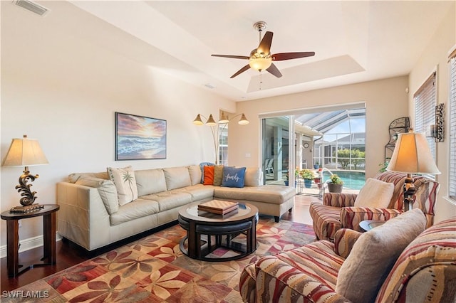 living area with ceiling fan, wood finished floors, a sunroom, visible vents, and a tray ceiling