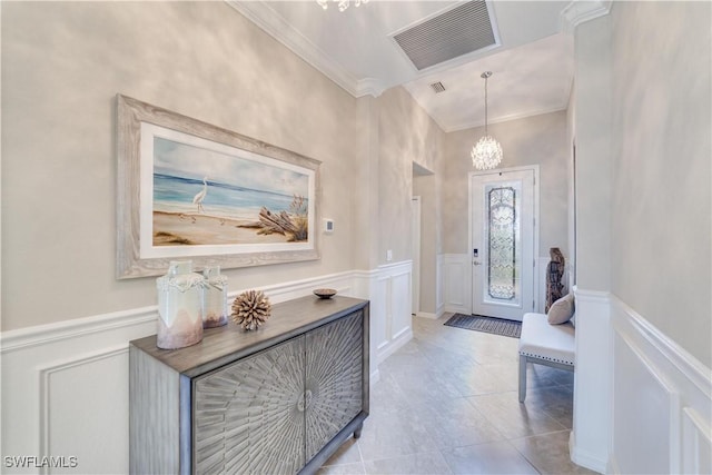 foyer with light tile patterned floors, visible vents, a wainscoted wall, ornamental molding, and a notable chandelier