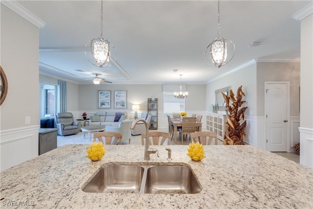 kitchen with a wainscoted wall, ornamental molding, open floor plan, light stone countertops, and a sink