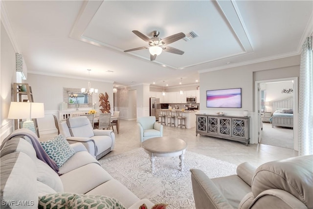 living area featuring crown molding, a raised ceiling, visible vents, wainscoting, and ceiling fan with notable chandelier