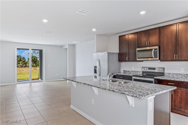 kitchen with appliances with stainless steel finishes, a sink, a breakfast bar area, a kitchen island with sink, and light stone counters